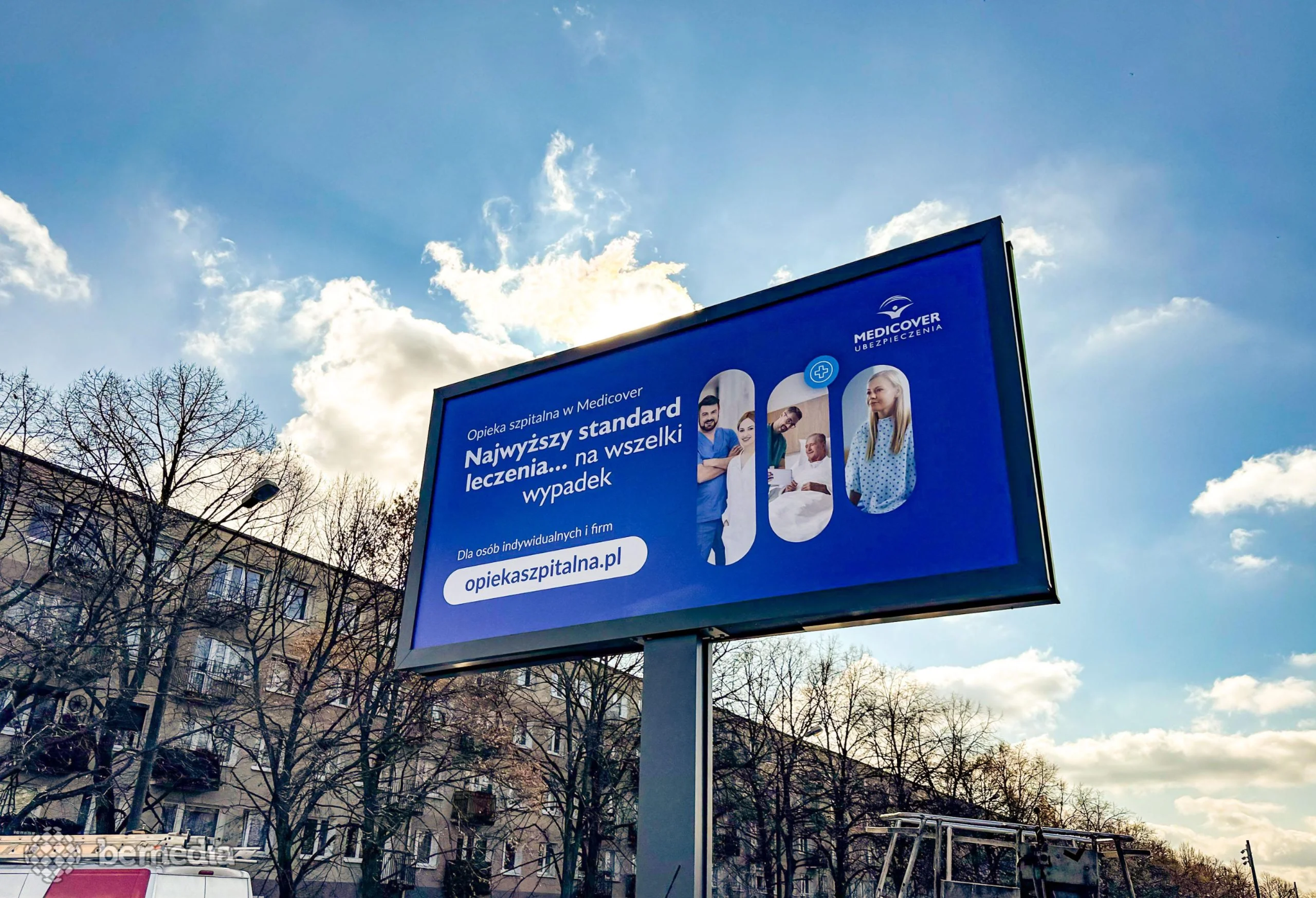  Large roadside billboard displaying a Medicover hospital care insurance advertisement against a blue sky.