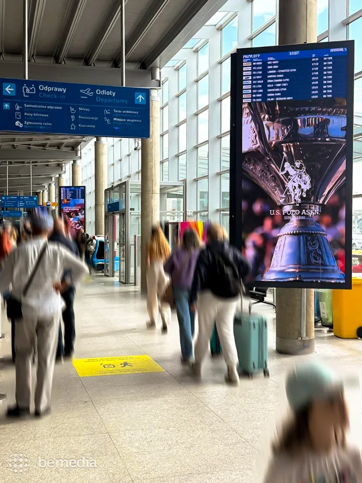 Digital advertising screen and departure signage inside a busy airport terminal