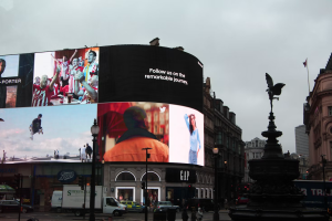 Large curved digital advertising screens displaying multiple campaigns at Piccadilly Circus in London.