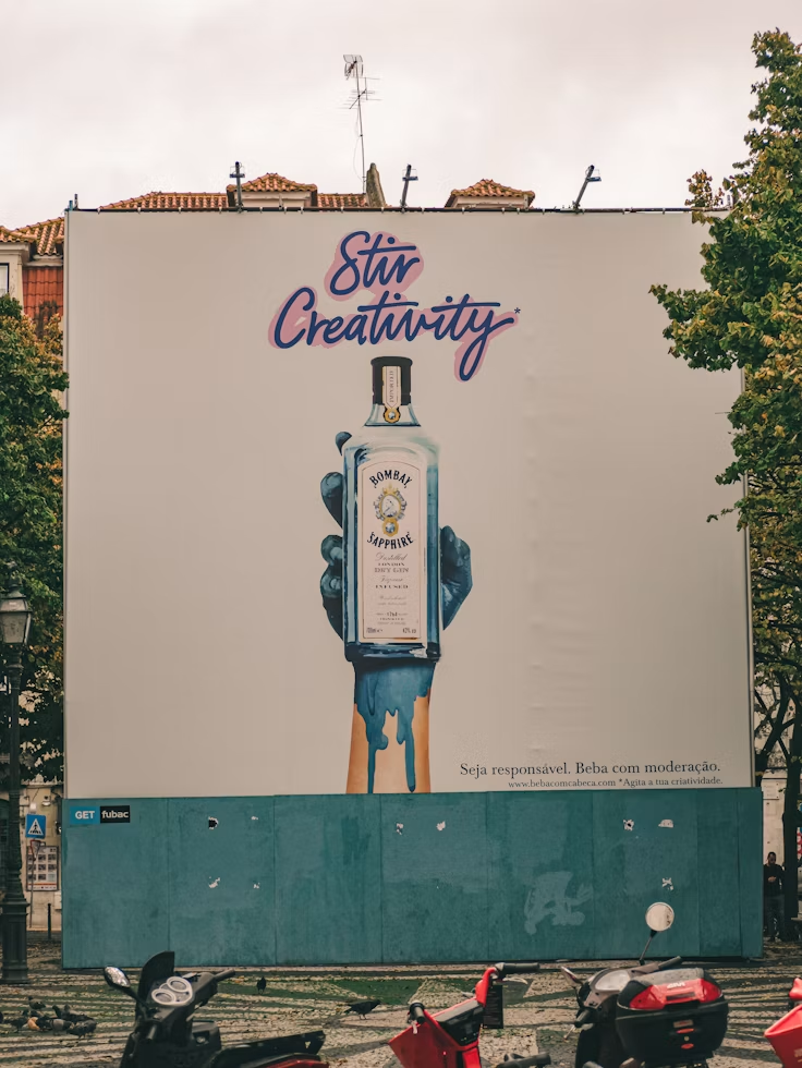 Large outdoor billboard featuring a Bombay Sapphire gin bottle held by a painted hand with the slogan “Stir Creativity.”