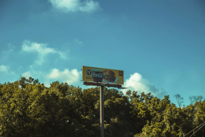Large roadside billboard displaying a fast-food advertisement above a tree-lined area