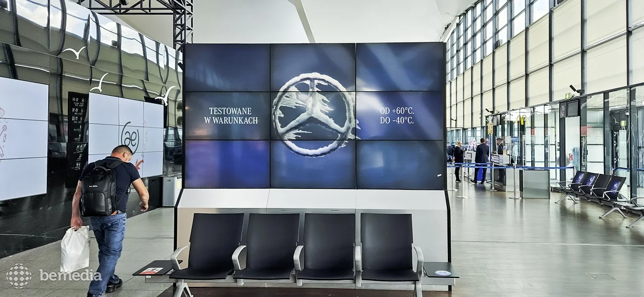 Large digital video wall displaying an advertisement above seating in an airport terminal.