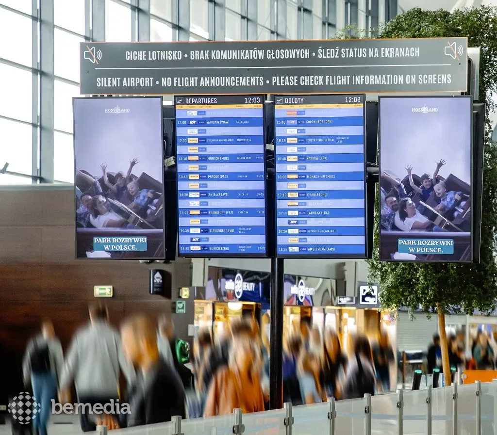 Airport departure information screens flanked by digital advertising displays in a busy terminal