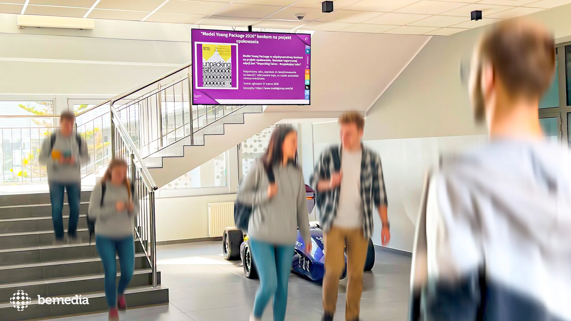 Ekran digital signage wyświetlający komunikat o konkursie Model Young Package 2026 w przestrzeni uczelni.