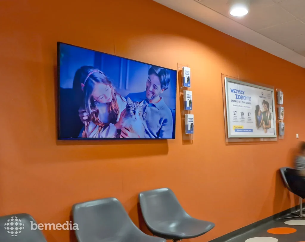 Ekran LCD z reklamą w poczekalni przychodni, nad krzesłami dla pacjentów